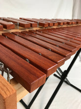 Load image into Gallery viewer, A close up picture of a xylophone with reddish brown wooden bars and metal posts on a black keyboard stand with a white background